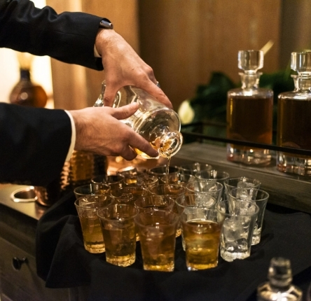a man pours whiskey into a series of shot glasses